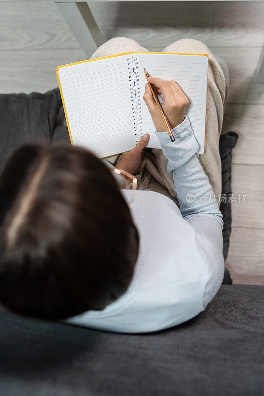 Top view on notebook in hands of unknown woman female student holding pencil ready to write on blank paper page while sitting on the floor at home - student taking notes during online class .(在线课堂上做笔记